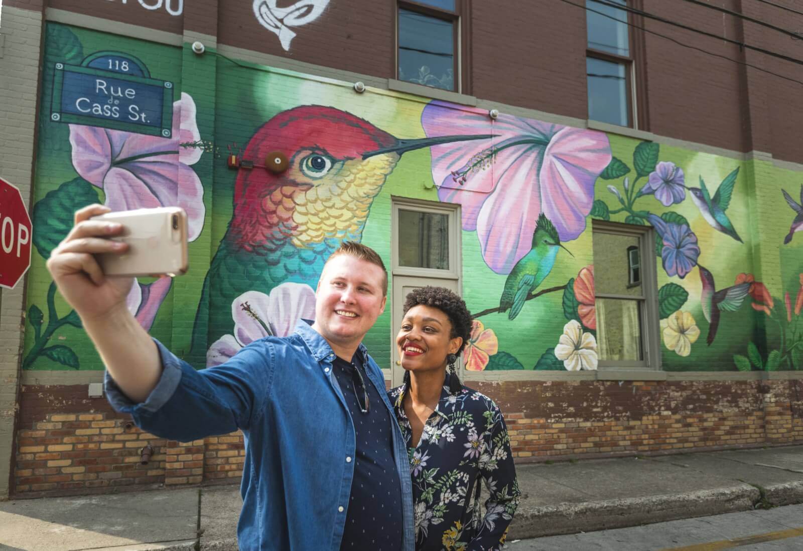 An interracial couple takes a selfie standing in front of a street mural in Traverse City, Michigan